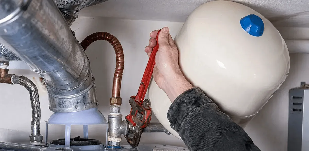 Water heater repair technician tightening plumbing connections near a tank unit in Fargo, ND